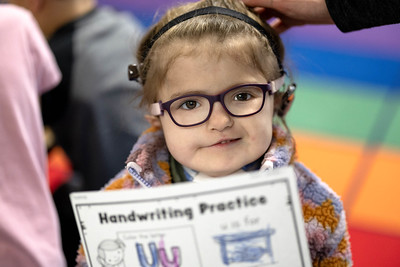 Young girl with glasses and headset with a copy of Handwriting Practice sheet