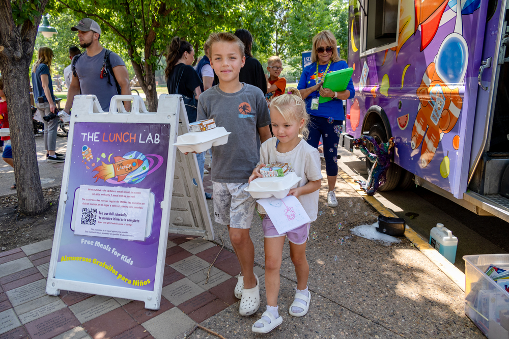 Two children walk away from a food truck carrying food boxes. 