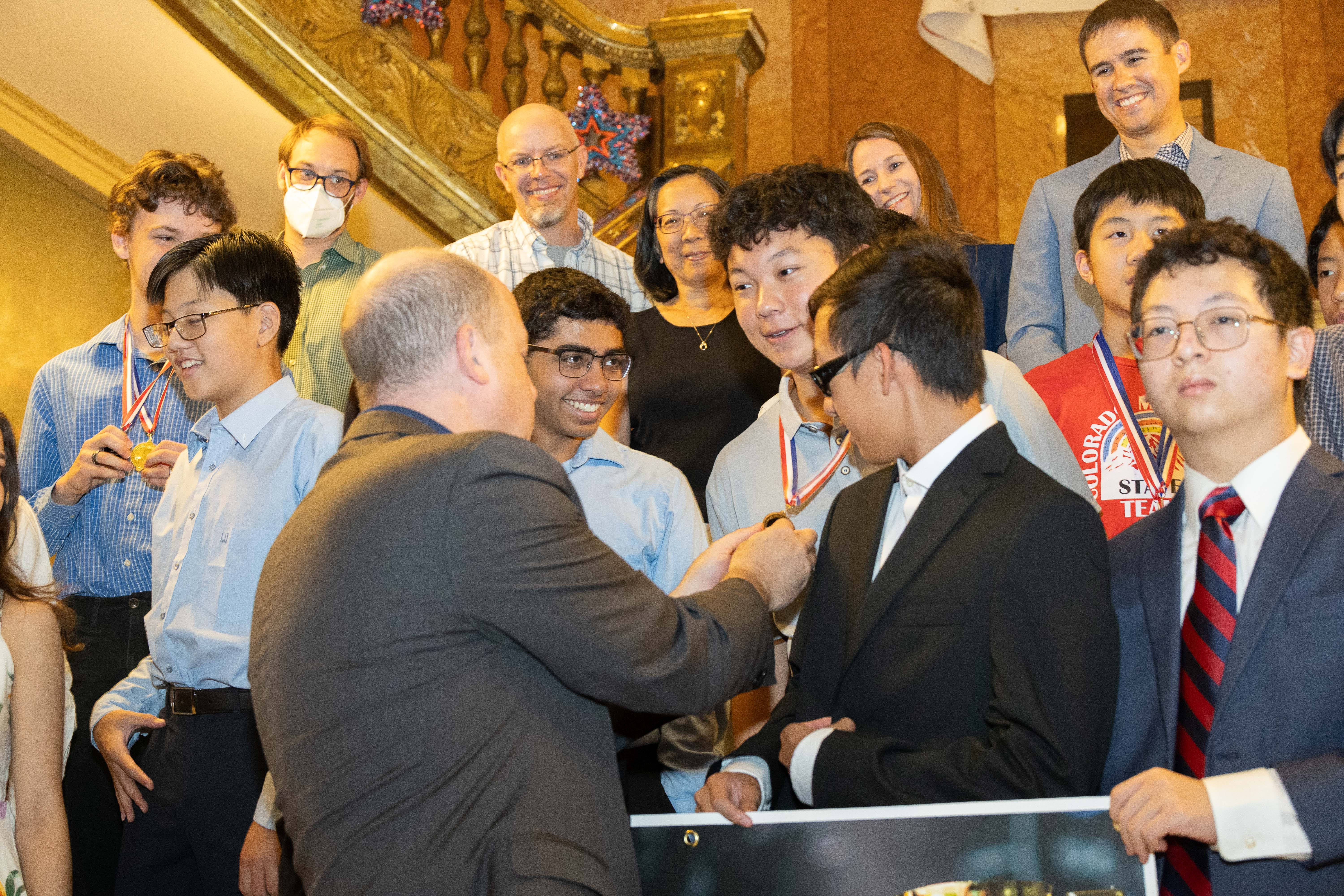 Gov. Jared Polis looks at a math award medal worn by a student. 