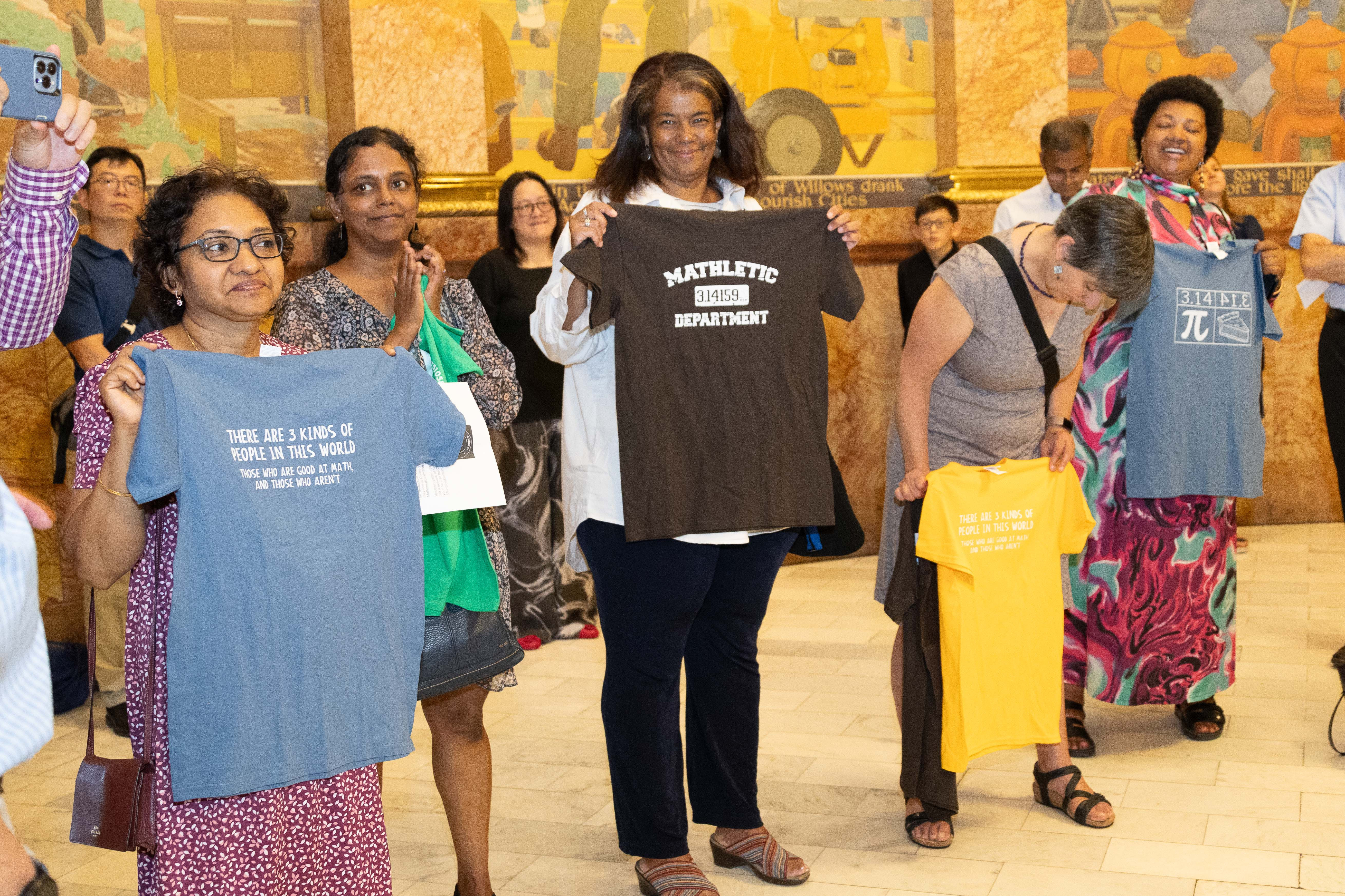 Four women hold up t-shirts with math puns in the capitol rotunda.