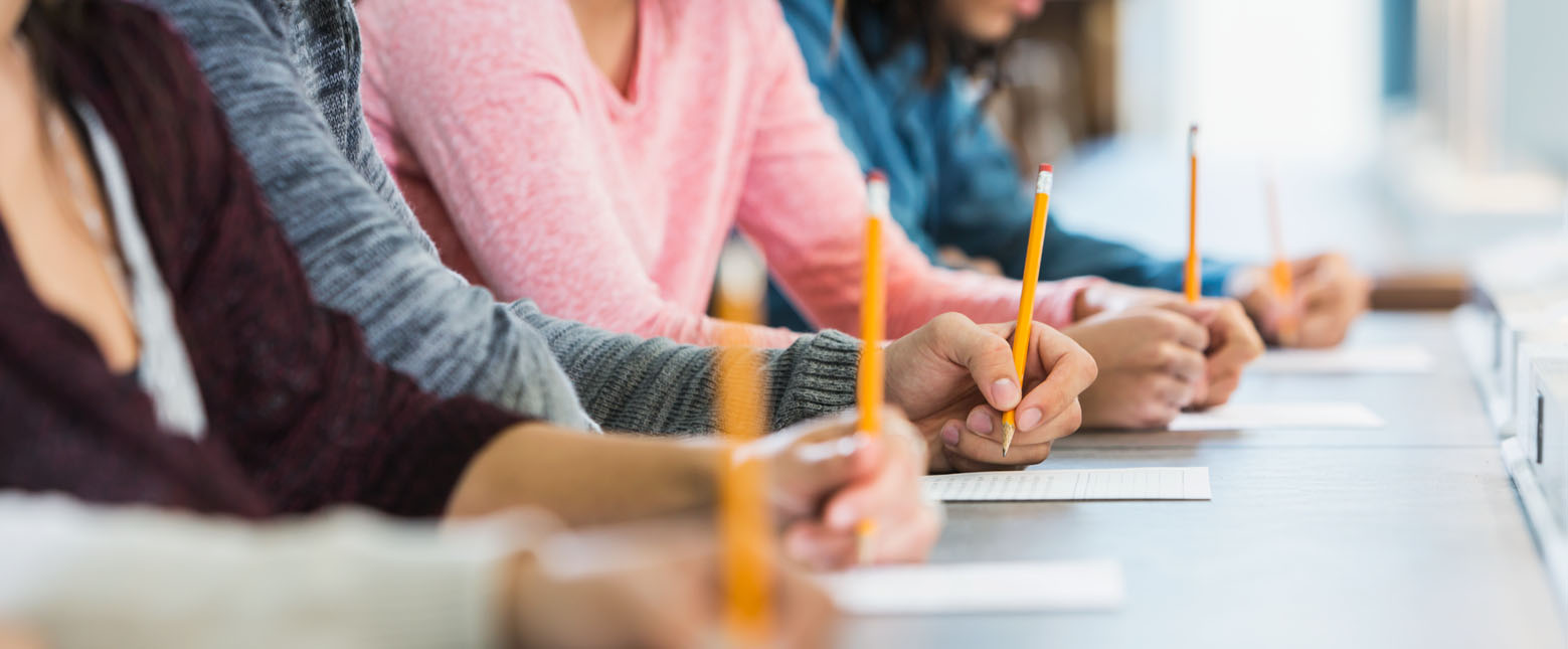 Row of people at a desk taking an exam with pencils in hand